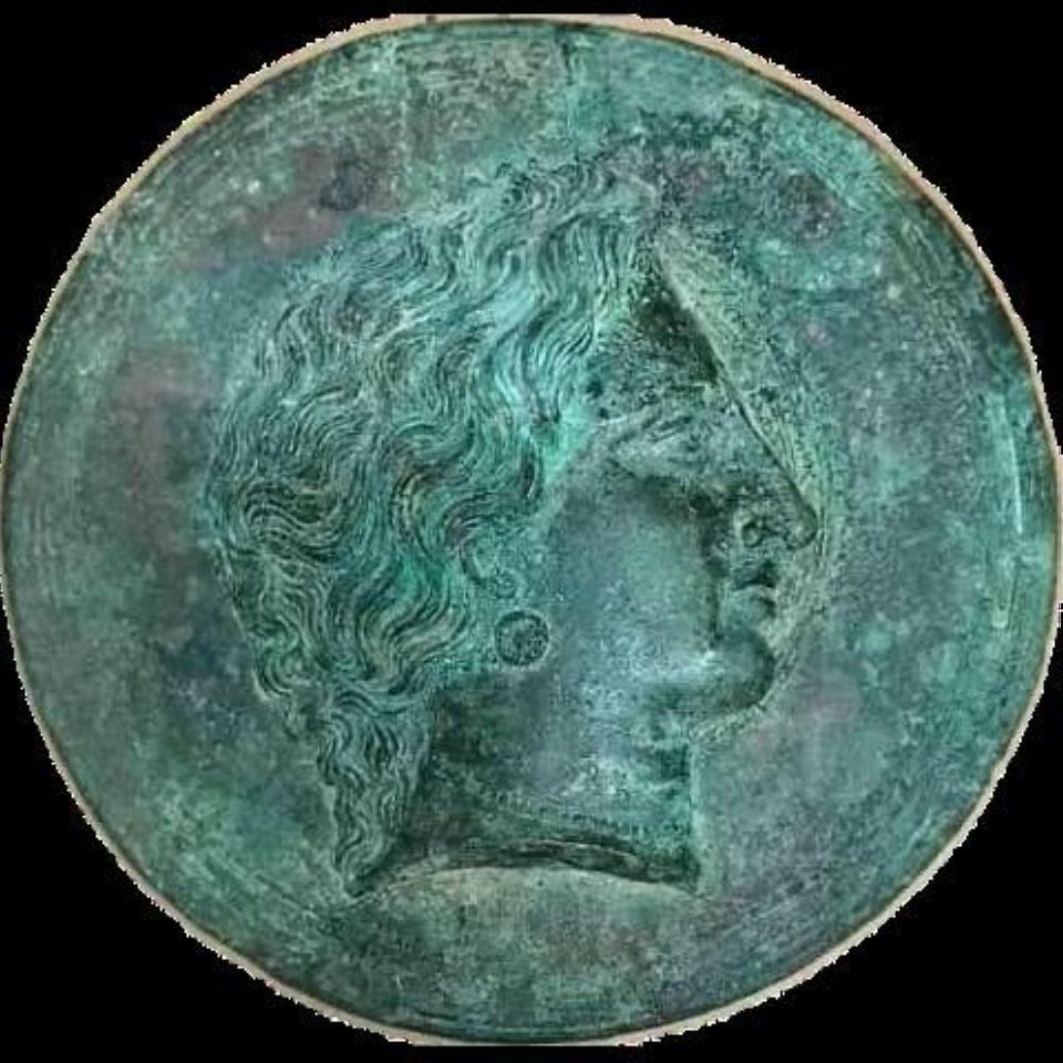 Χάλκινος δίσκος κατόπτρου. Φέρει στο κάλυμμα ανάγλυφη διακόσμηση γυναικείας κεφαλής σε κατατομή. Διάμετρος 15,20 εκ. Γύρω στα 270-260 π.Χ.