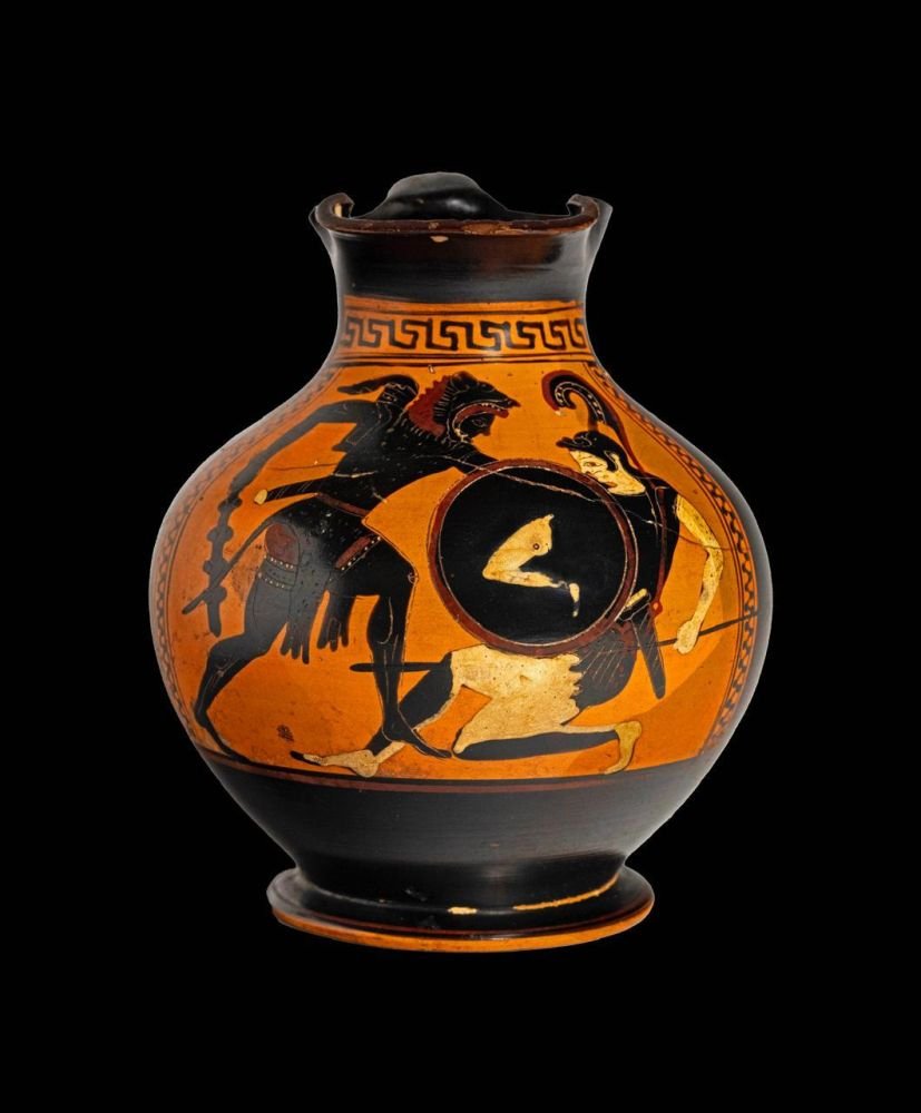 Αττικός μελανόμορφος χους με σκηνή μάχης ανάμεσα στον Ηρακλή και σε Αμαζόνα. Ο Ηρακλής επιτίθεται με ρόπαλο. Η αμυνόμενη Αμαζόνα φέρει κορινθιακό κράνος με υψηλό λοφίο και κρατά δόρυ και ασπίδα με ανθρώπινο σκέλος ως επίσημα. Ύψος 15,15 εκ. 550-500 π.Χ.