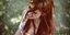 Γυναίκα με κόκκινα μαλλιά χαμογελάει καθισμένη στο γρασίδι