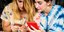 Δύο γυναίκες με πολύχρωμα ρούχα κοιτούν το κινητό τους 