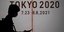 Ανθρωπος στη σκιά με κινητό στο χέρι περνάει από σήμα με Ολυμπιακούς Αγώνες Τόκιο 
