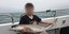 O 18χρονος χάκερ που διέρρευσε υλικό από το Grand Theft Auto 6, κρατάει ένα ψάρι ενώ κάθεται σε βάρκα, με θολωμένο πρόσωπο
