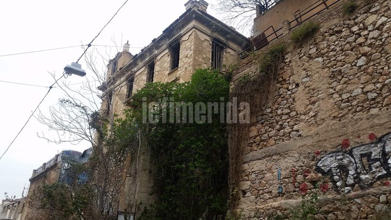 Το πέτρινο σπίτι από την πλαϊνή πλευρά με γκράφιτι στο κάτω μέρος.