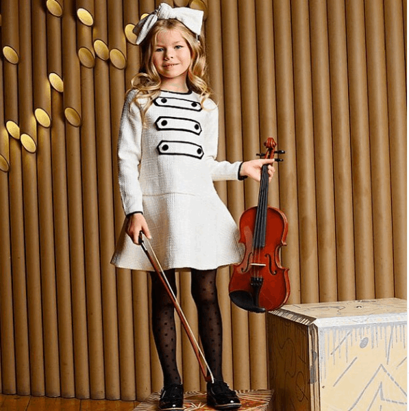 6χρονο μοντέλο με λευκό φόρεμα κρατώντας ένα βιολί 