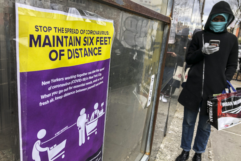Άνδρας με μάσκα μπροστά σε πινακιδα με απόσταση ασφαλείας για κορωνοϊό