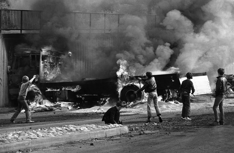 Πιτσιρίκια πετούν πέτρες σε ένα φορτηγό που καίγεται στο Λόντονερι της Βόρειας Ιρλανδίας, στις ταραχές μετά τον θάνατο του Μπόμπι Σαντς, Μάιος 1981. Φωτογραφία: AP Photo/David Caulkin.