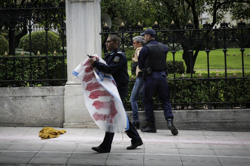 Οι αστυνομικοί την ακινητοποιούν και κρατούν το πανό στα χέρια τους- φωτογραφία eurokinissi