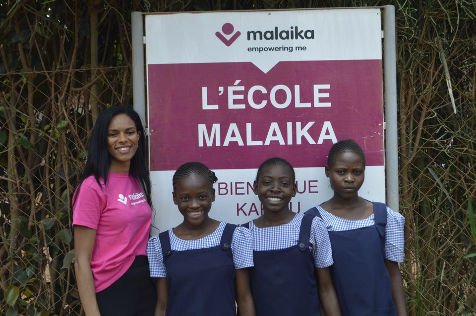 Η Noella με μαθήτριες μπροστά από πινακίδα του σχολείου από τη Malaika