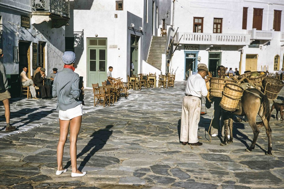 Γαλλίδα τουρίστρια φωτογραφίζει Μυκονιάτη έμπορο να ζεύγει τον γάιδαρό του με προμήθειες, 1957