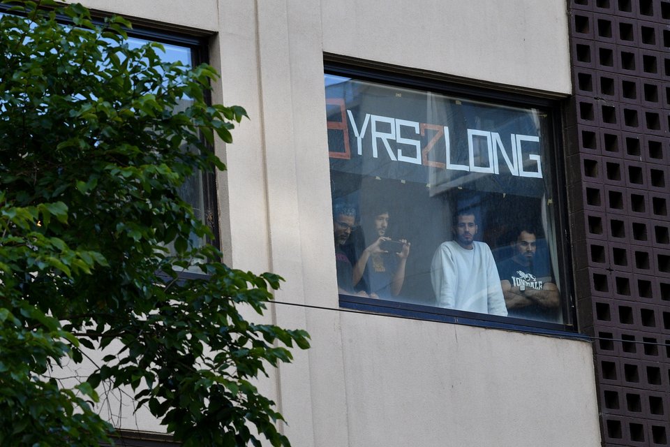 Πρόσφυγες παρακολουθούν από τα παράθυρα τις κάμερες των ΜΜΕ που έχουν συγκεντρωθεί από έξω