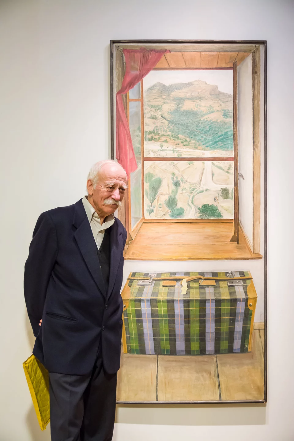 Ο Χρόνης Μπότσογλου μπροστά σε έργο του όπου αποτυπώσε τη θέα που έβλεπε από το παράθυρό του στο σπίτι του στο Πετρί της Μυτιλήνης / ΜΙΕΤ