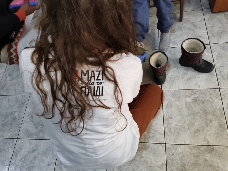 Εθελόντρια από το Μαζί για το Παιδί βοηθά ένα παιδί να δοκιμάσει παπούτσια