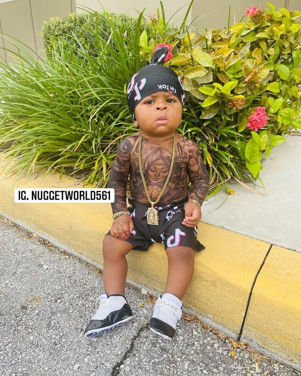 το αγοράκι ποζάρει με τατουάζ στο στήθος, μπαντάνα και χρυσό κολιέ