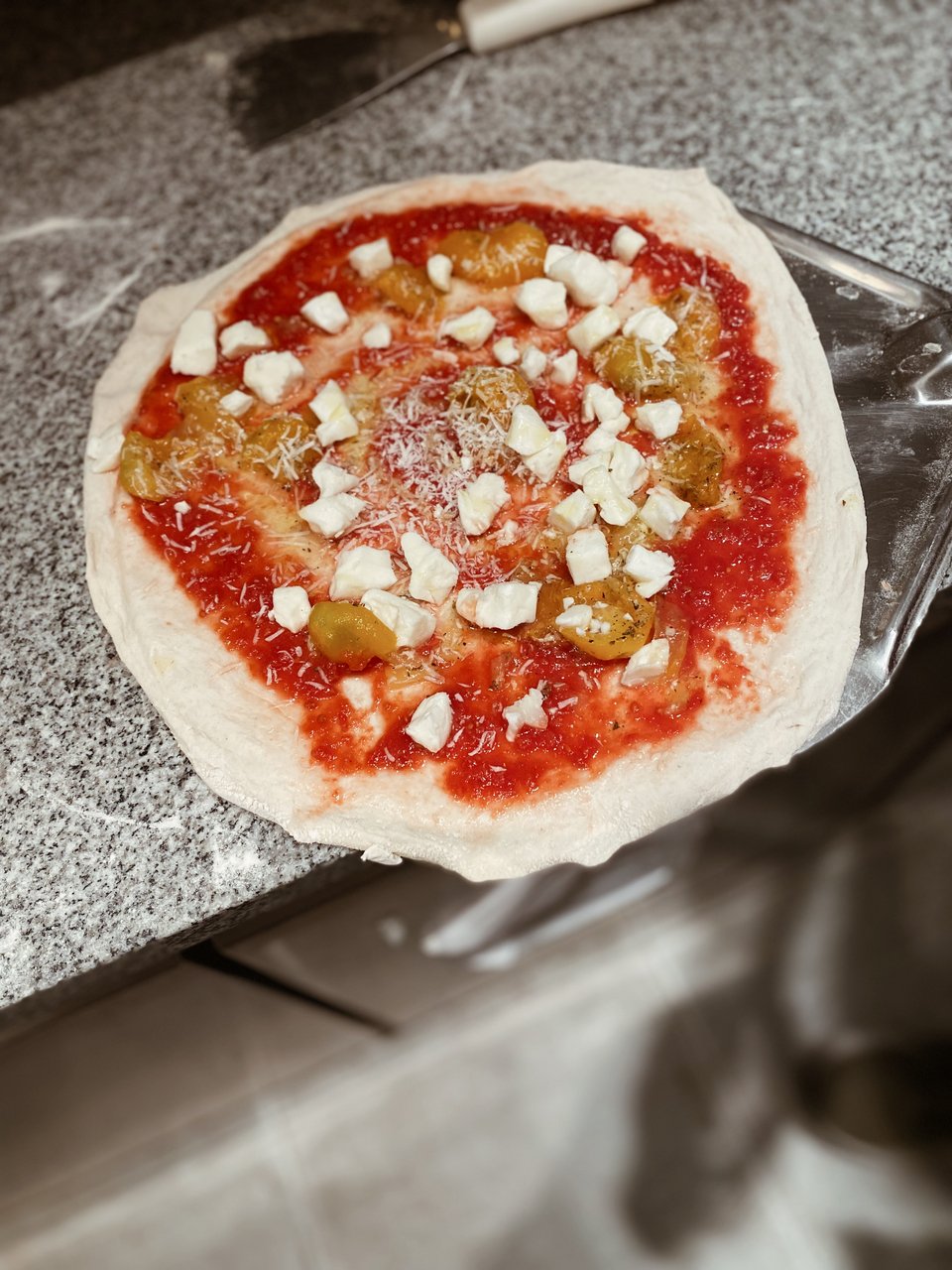 Ο σεφ προσθέτει κομμάτια μοτσαρέλας πριν βάλει τη Μαργαρίτα στο φούρνο. 