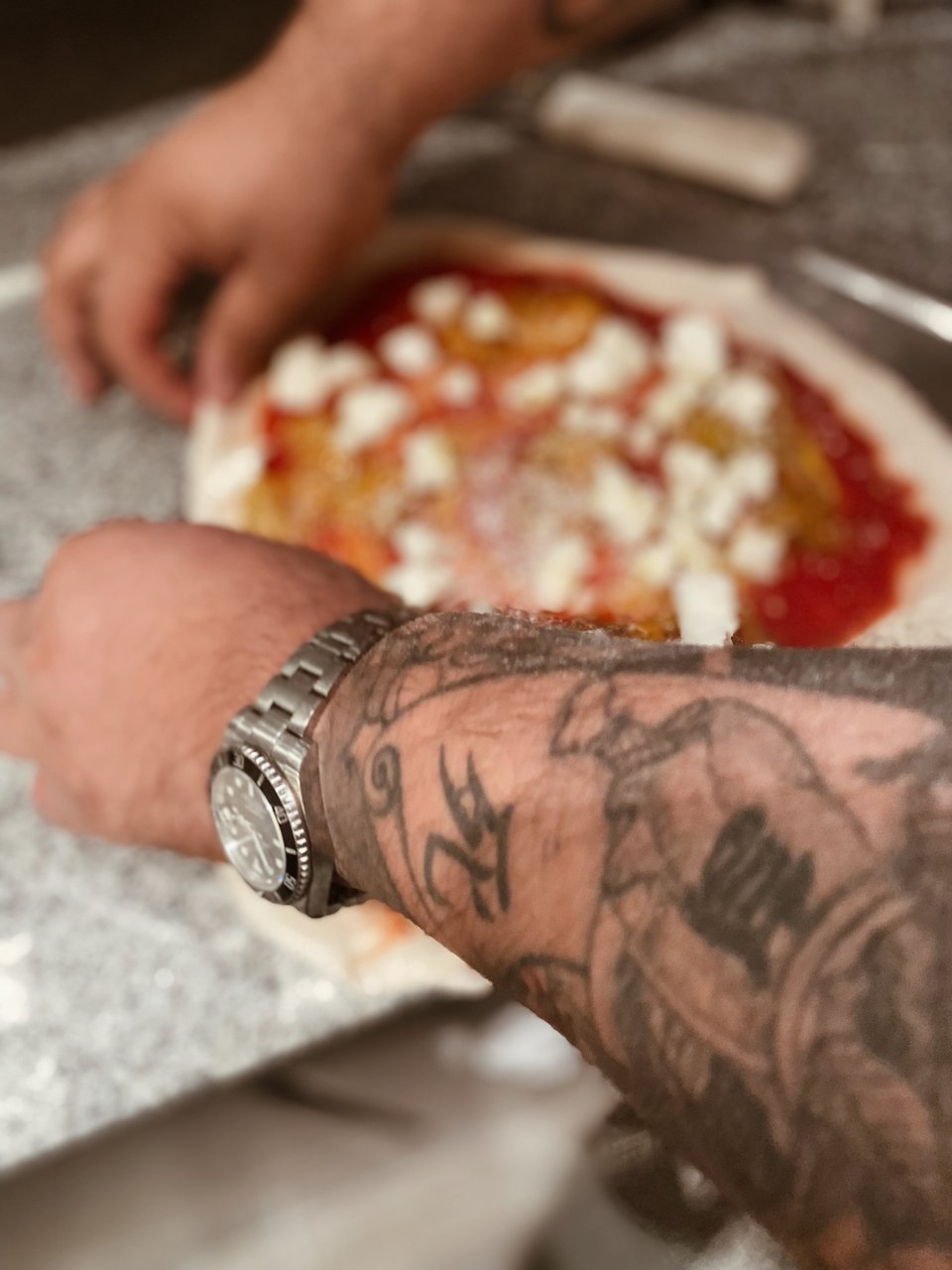 Ο Μάρκο τραβάει τις άκρες της ζύμης για να ανοίξουν περισσότερο πάνω στο φτυάρι ψησίματος. 