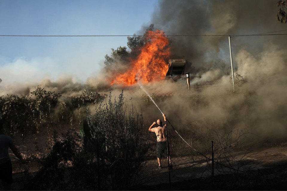 Κάτοικοι με μάνικες και λάστιχα καταβρέχουν στέγες σπιτιών για να περιορίσουν τις ζημιές από τη φωτιά 