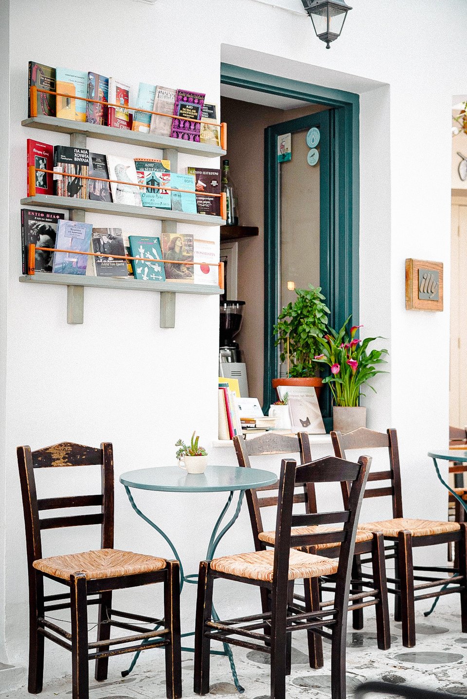 Έξω από το βιβλιοπωλείο Αντίλαλος, στο λευκό ασβεστωμένο σοκάκι, έχουν τοποθετηθεί τραπεζάκια με καρέκλες καφενείου για διάβασμα με συνοδεία καφέ, ποτού ή φαγητού. 