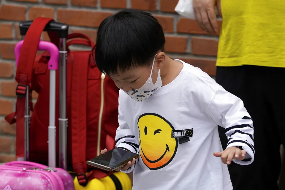 Ένα παιδί που φοράει μάσκα στην Κίνα παίζει παιχνίδι σε ένα smartphone