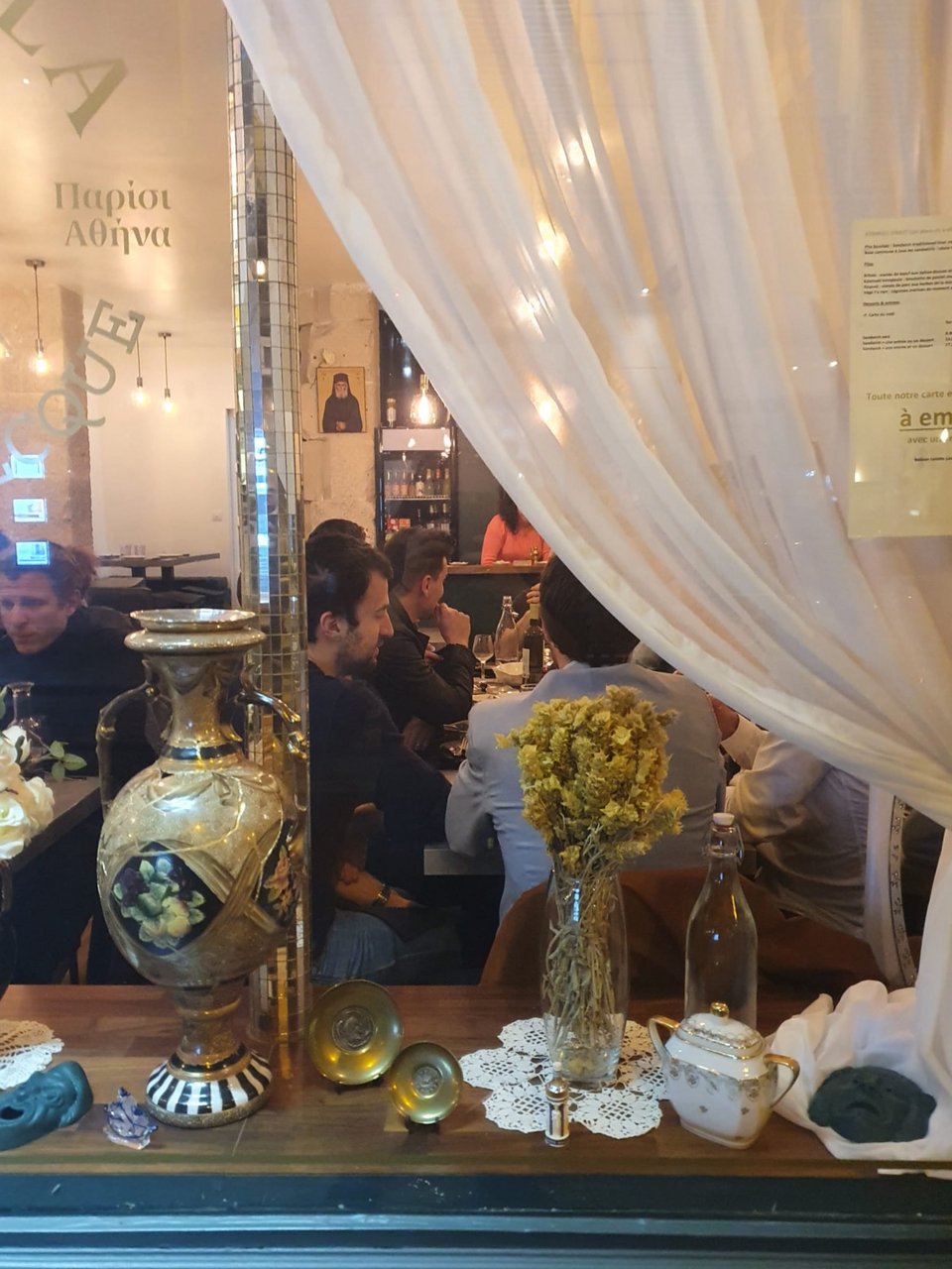 Στη βιτρίνα του εστιατορίου παλιά βάζα, μπιμπελό και δαντελένια σεμέν δίνουν το στίγμα της διακόσμησης που παραπέμπει σε vintage διαμέρισμα της Αθήνας. 