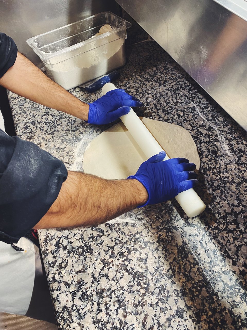 Με έναν χοντρό πλάστη ανοίγεται το ζυμάρι της πίτσας. 