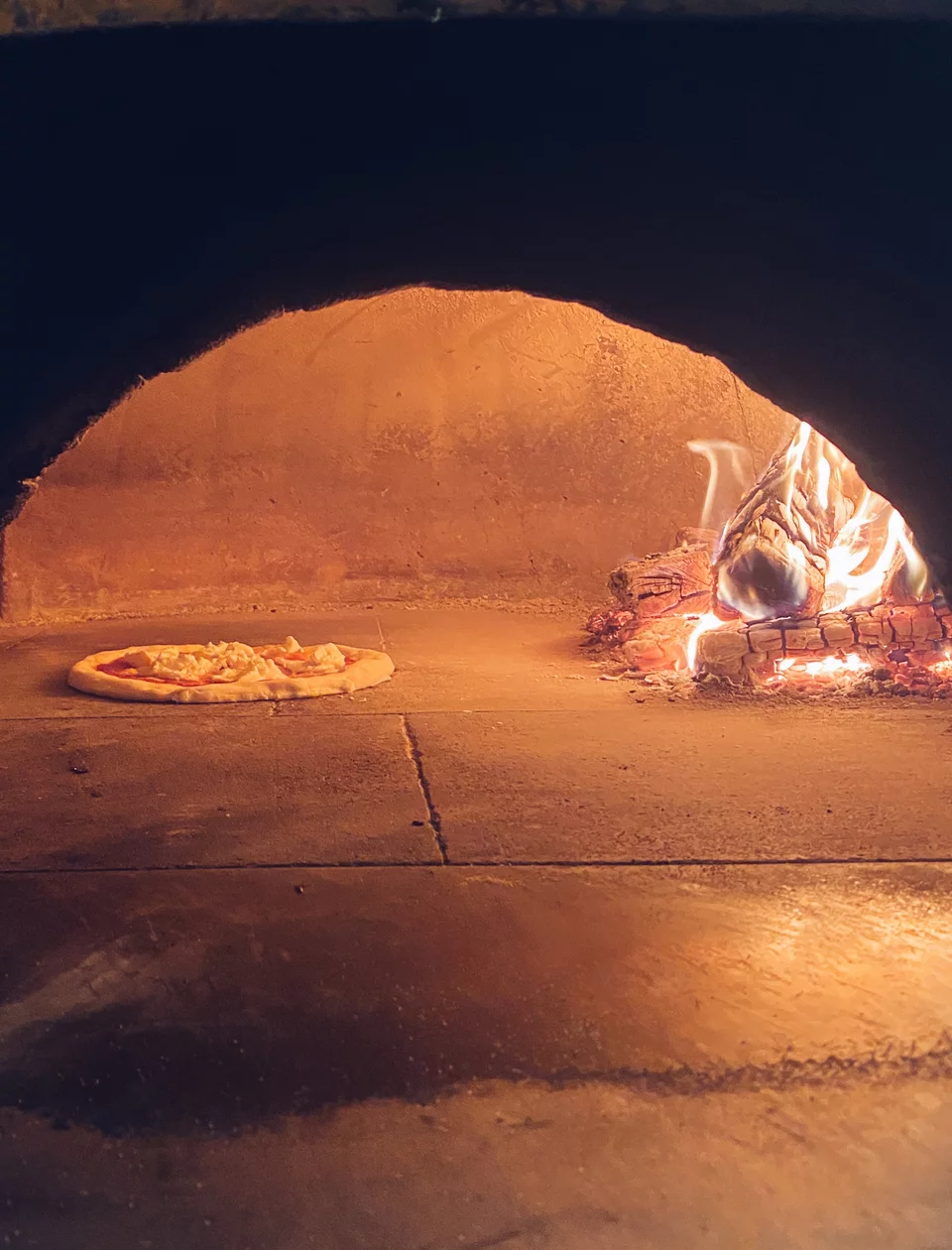 Η πίτσα ψήνεται ομοιόμορφα πάνω στην πυρωμένη πέτρα του ξυλόφουρνου.