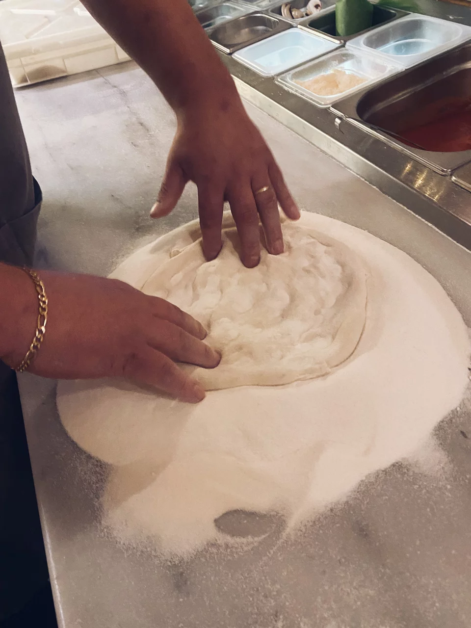 Το μπαλάκι της ζύμης ανοίγεται με πιέσεις των δακτύλων πάνω στο αλεύρι που έχουμε ρίξει στον πάγκο.