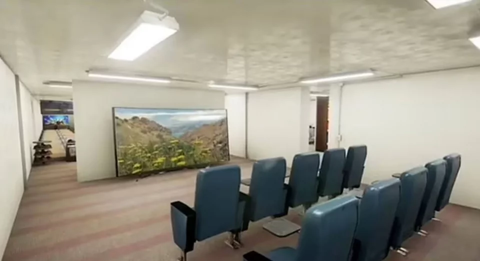 Μια κινηματογραφική αίθουσα σε ένα πολυτελές καταφύγιο επιβίωσης Rising S. Στο βάθος, διακρίνεται μια αίθουσα μπόουλινγκ.