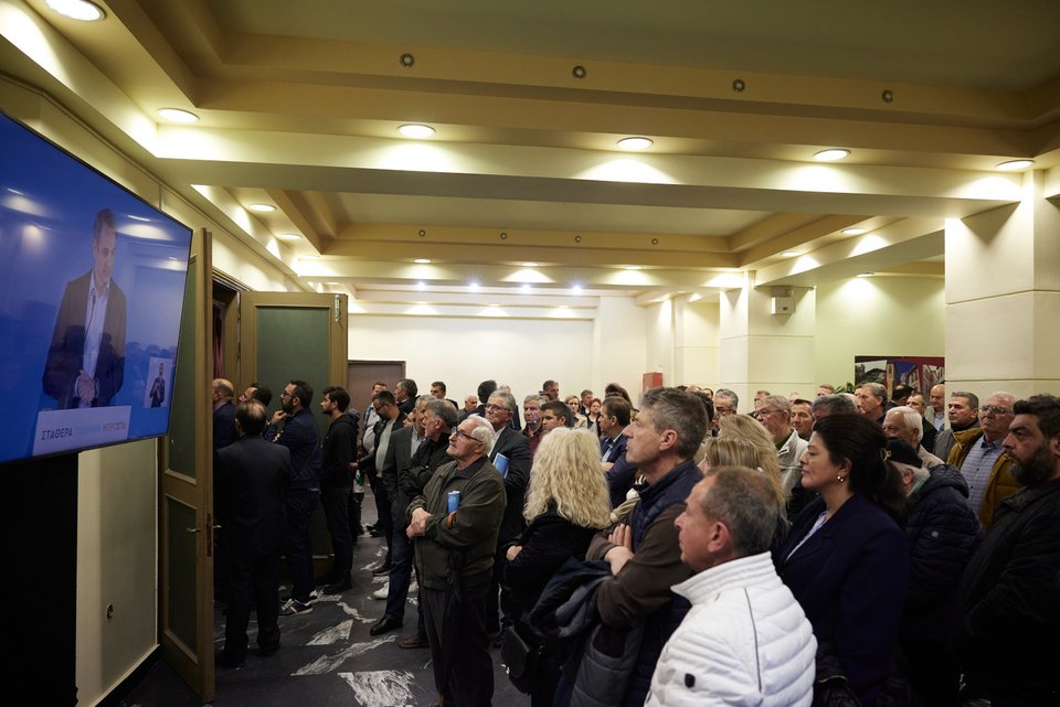 Κόσμος βλέπει από οθόνη την ομιλία Μητσοτάκη έξω από την αίθουσα