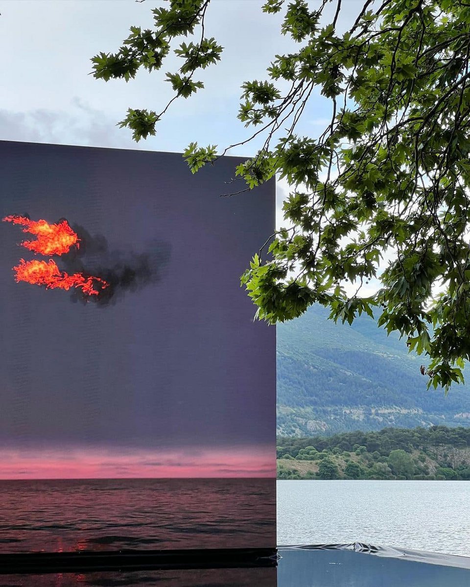 Flare (Oceania) του John Gerrard. H οθόνη με την φλεγόμενη σημαία «πατάει» σε μία επιφάνεια νερού, ακριβώς πάνω από τη λίμνη. Στα εγκαίνια ταυτόχρονα έβρεχε -ένας υδάτινος κυκλωτικός κλοιός./ Βασίλης Μπίμπας