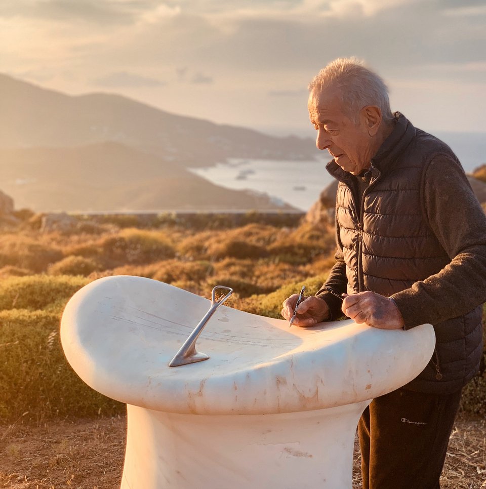 O Mηνάς στο χωράφι γύρω από το σπίτι, μπροστά σε ένα ηλιακό ρολόι που σχεδίασε και έφτιαξε με τα χέρια του
