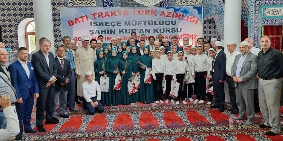 Ο Χουσεΐν Ζεϊμπέκ ποζάρει μπροστά από πανό με σαφή αναφορά στην «Τουρκική μειονότητα της Θράκης»