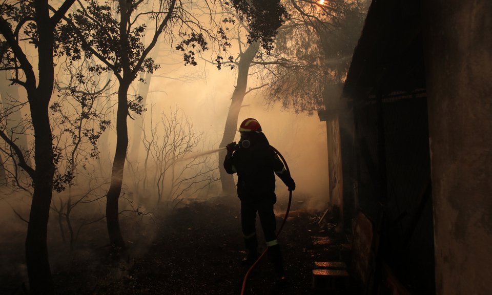 Πυροσβέστης ρίχνει νερό έξω από καμμενο σπίτι