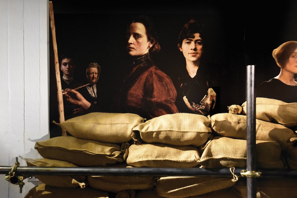 Το κολάζ των γυναικών-δημιουργών του έργου με τα σακιά άμμου και το σιδερένιο πλαίσιο/σκαλωσιά που τις κρατά σε απόσταση