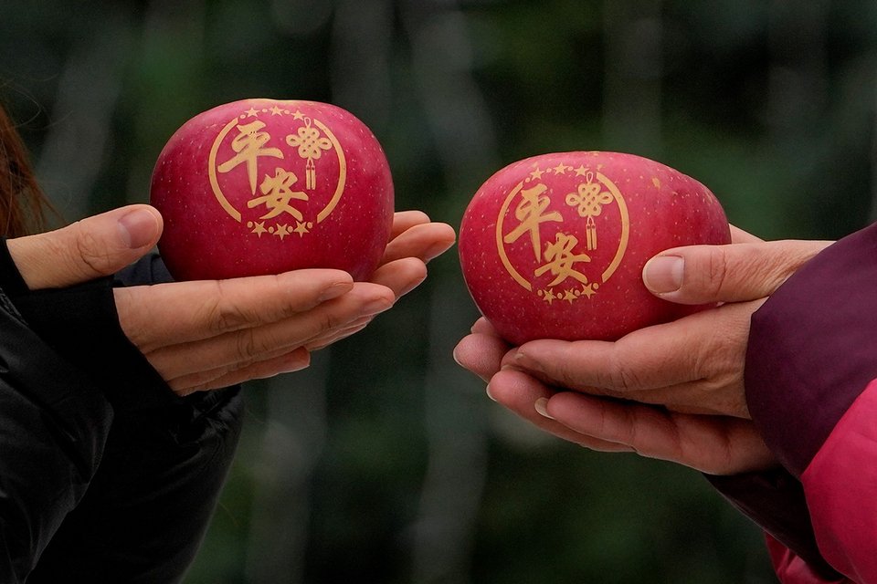 Γυναίκες κρατούν μήλα με κινεζικούς χαρακτήρες που σημαίνουν «ειρήνη» καθώς ποζάρουν μπροστά από ένα χριστουγεννιάτικο δέντρο στολισμένο έξω από καθολική εκκλησία, την παραμονή των Χριστουγέννων στο Πεκίνο / AP Photo/Andy Wong)