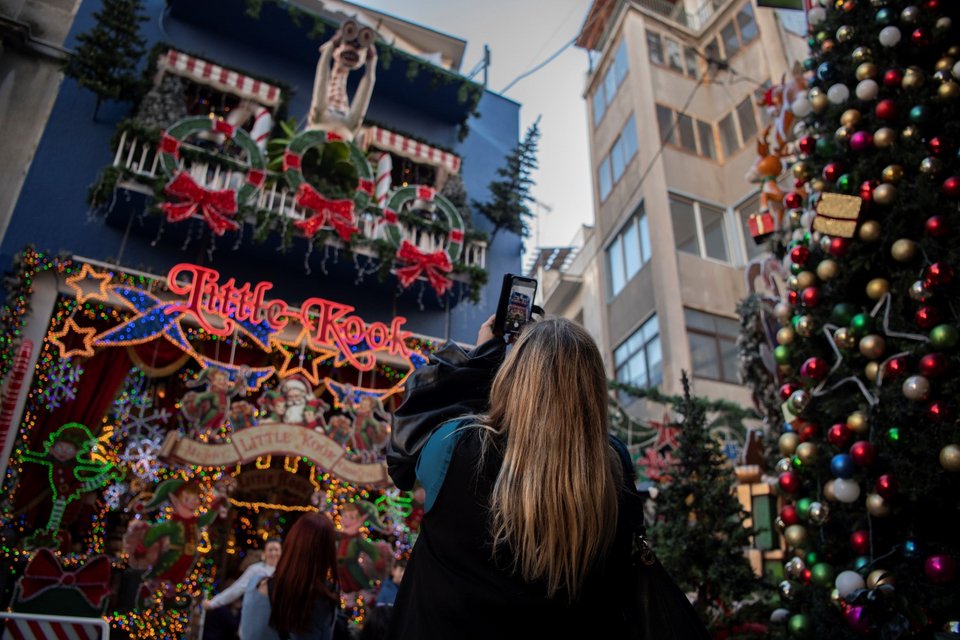 Μια γυναίκα τραβάει φωτογραφίες με το τηλέφωνό της στην περιοχή του Ψυρρή στην Αθήνα, την παραμονή των Χριστουγέννων / AP Photo/Michael Varaklas