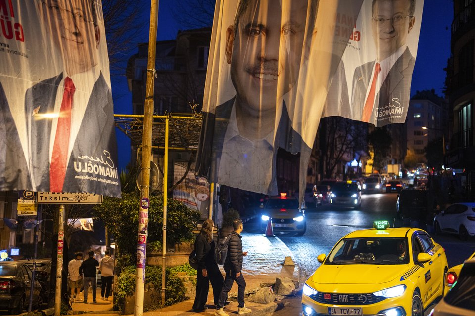 Άνθρωποι περπατούν κάτω από τα προεκλογικά πανό των υποψηφίων για την Κωνσταντινούπολη Ekrem Imamoglu και Murat Kurum