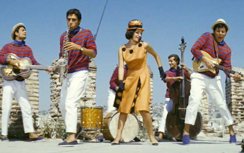 Στον Λευκό Πύργο, το εμβληματικό τοπόσημο της Θεσσαλονίκης, η Μάρθα Καραγιάννη χορεύει στην ταράτσα, στον ρυθμό της μπάντας του Κώστα Βουτσά, στη γνωστή ταινία «Κάτι να καίει»