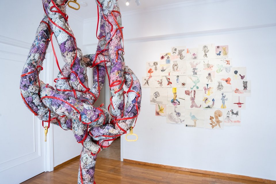 Φωτογραφία εγκατάστασης Μυθιστορίες ΙΙ. Νάνα Σαχίνη, who knows what the “and” stands for: story of an acrobat, 2014, 240 x 100 x 80 εκ., papier-mache, χρώμα, συρματόπλεγμα, φωτογραφίες performance, τσιμέντο, πλαστικό καλώδιο (αριστερά). Νάνα Σαχίνη, the Bible of dreams, 2007 – σε εξέλιξη, διαστάσεις μεταβλητές, μικτή τεχνική σε χειροποίητο χαρτί (δεξιά). Παραχώρηση του καλλιτέχνη και της CITRONNE Gallery © Alexandra Masmanidi