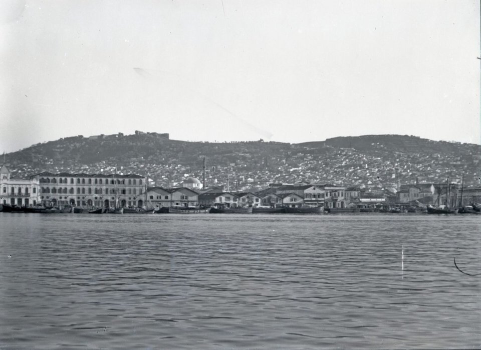 Σμύρνη, 1921-1922. Γενική άποψη της ακτογραμμής, πόλης και προκυμαίας – Quais, από την Εθνική Τράπεζα της Ελλάδος (αριστερά) ως το Τελωνείο (δεξιά). Στο βάθος διακρίνεται η ακρόπολη του Πάγου με το μεσαιωνικό κάστρο (Φωτογραφικό Αρχείο Εθνικού Αρχαιολογικού Μουσείου)