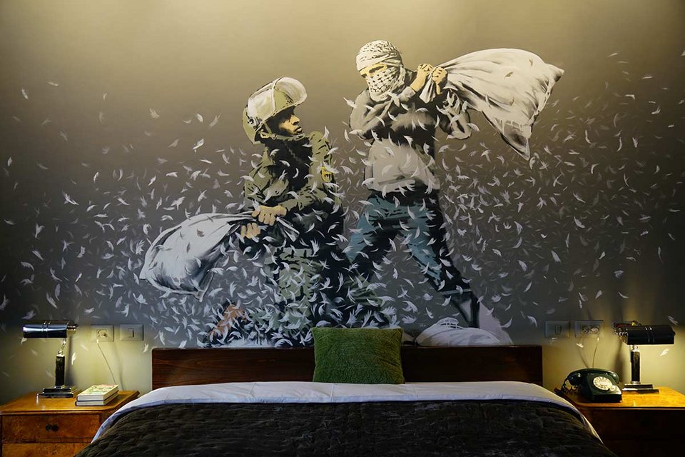 Ένα king-size κρεβάτι κάτω από το έργο τέχνης του Banksy που δείχνει έναν Παλαιστίνιο και έναν Ισραηλινό σε μαξιλαροπόλεμο / WIKIPEDIA