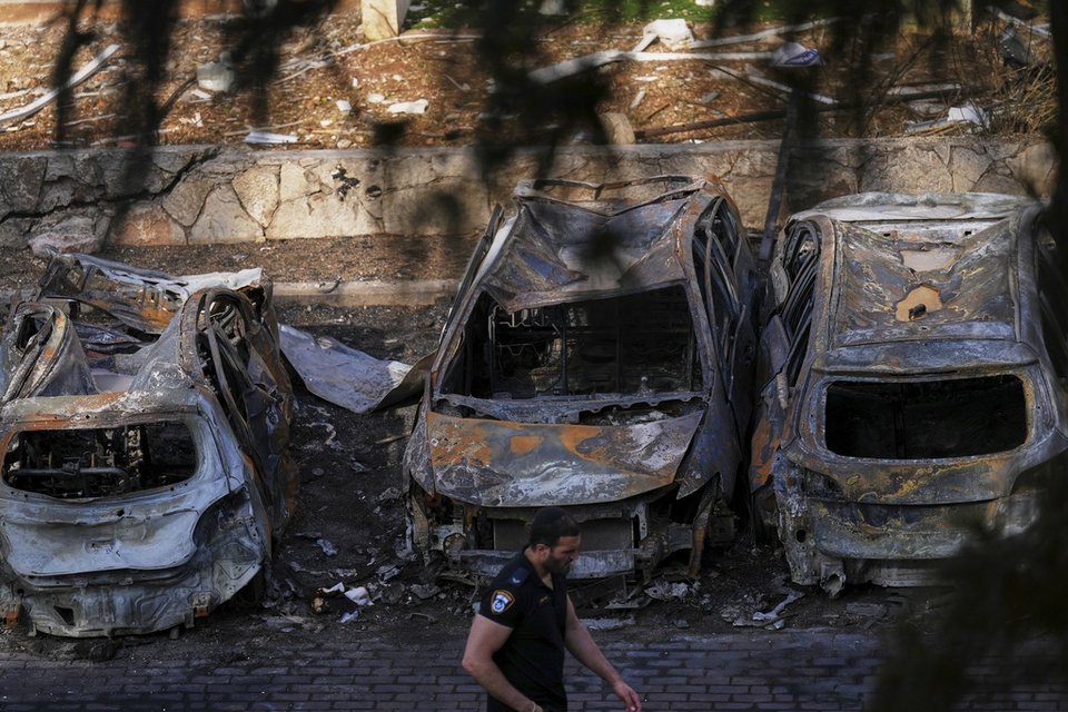 Ένας αστυνομικός περπατά δίπλα από καμένα οχήματα στο σημείο όπου έπεσε ιρανικός πύραυλος στη Χάιφα του Ισραήλ, Δευτέρα 16 Ιουνίου 2025. (AP Photo/Ariel Schalit)