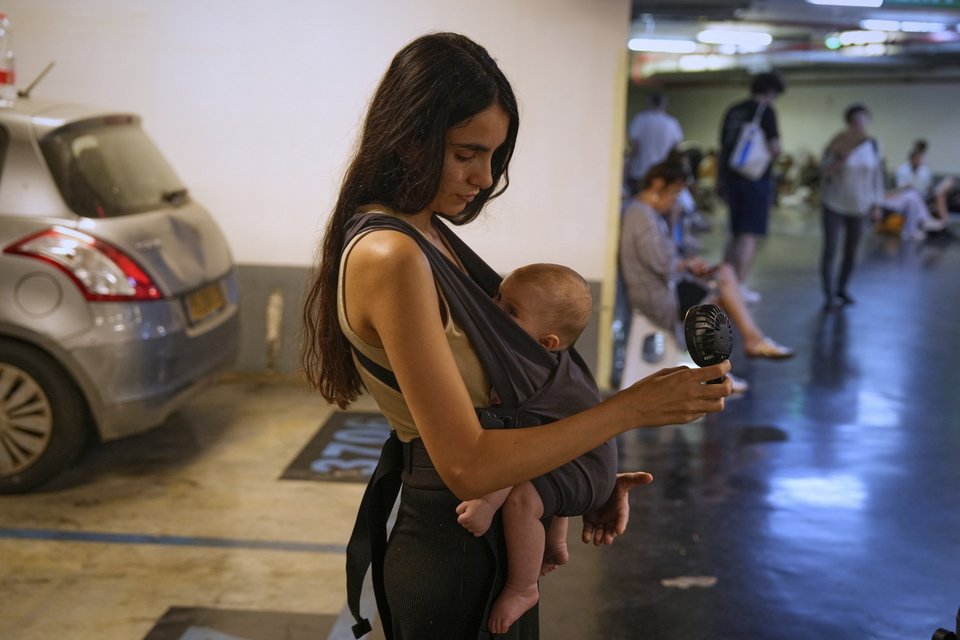 Μια γυναίκα κρατάει έναν φορητό ανεμιστήρα για να δροσίσει το μωρό της καθώς Ισραηλινοί βρίσκουν καταφύγιο σε ένα πάρκινγκ κατά τη διάρκεια συναγερμού για πυραύλους από το Ιράν, στο Τελ Αβίβ του Ισραήλ, Κυριακή 15 Ιουνίου 2025. / Φωτογραφία AP