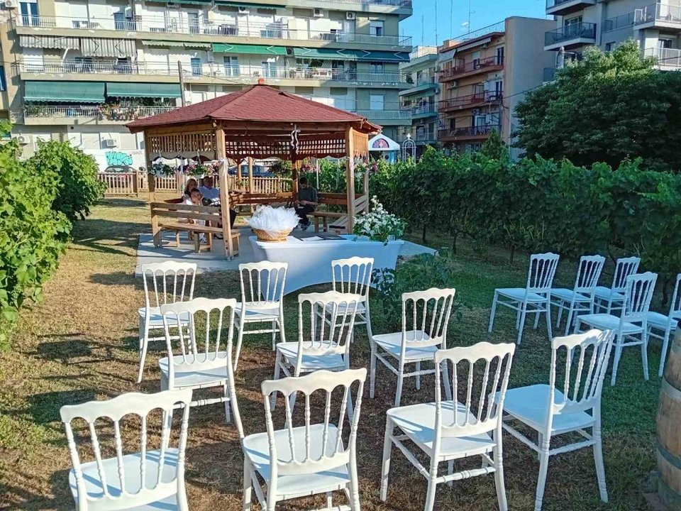 Το σκηνικό θυμίζει κινηματογραφική ταινία με τις άσπρες καρέκλες να είναι στοιχισμένες, αφήνοντας ένα διάδρομο μέσα στο φυσικό περιβάλλον για να σταθεί το ζευγάρι