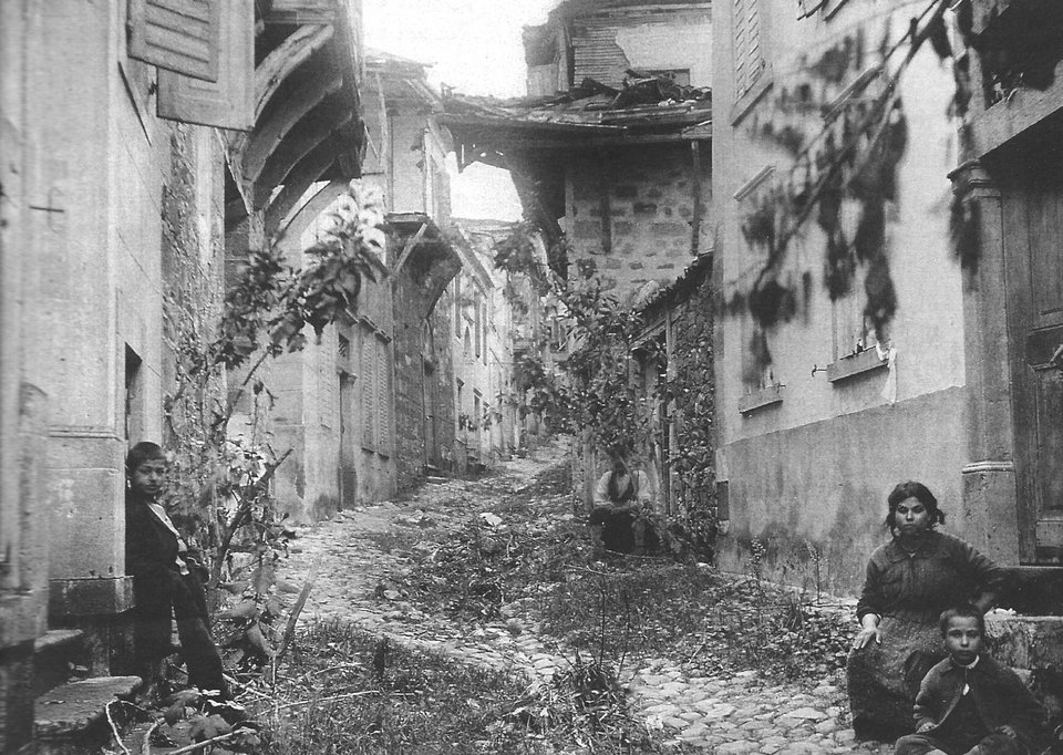 Ο δρόμος προς το Ναό της Παναγίας το 1919, μετά την επιστροφή στο Μοσχονήσι των κατοίκων του που το είχαν εγκαταλείψει στο λεγόμενο Α Διωγμό του 1914. Φανερές οι ζημιές στα σπίτια. Αρχείο Α. Μαϊλη 1919