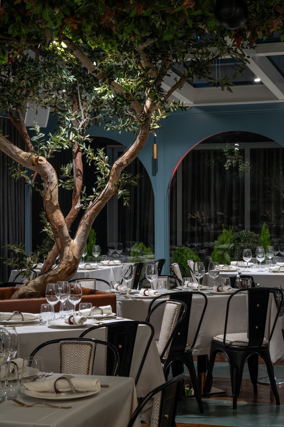 Καμάρες, γαλάζιο χρώμα, λευκά τραπεζομάντιλα και μια ελιά στην καρδιά της σάλας του Sea You στο Κολωνάκι. 