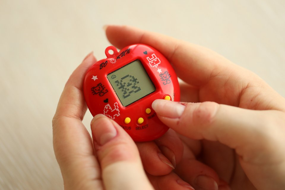 Χέρια κρατούν ένα κόκκινα tamagotchi