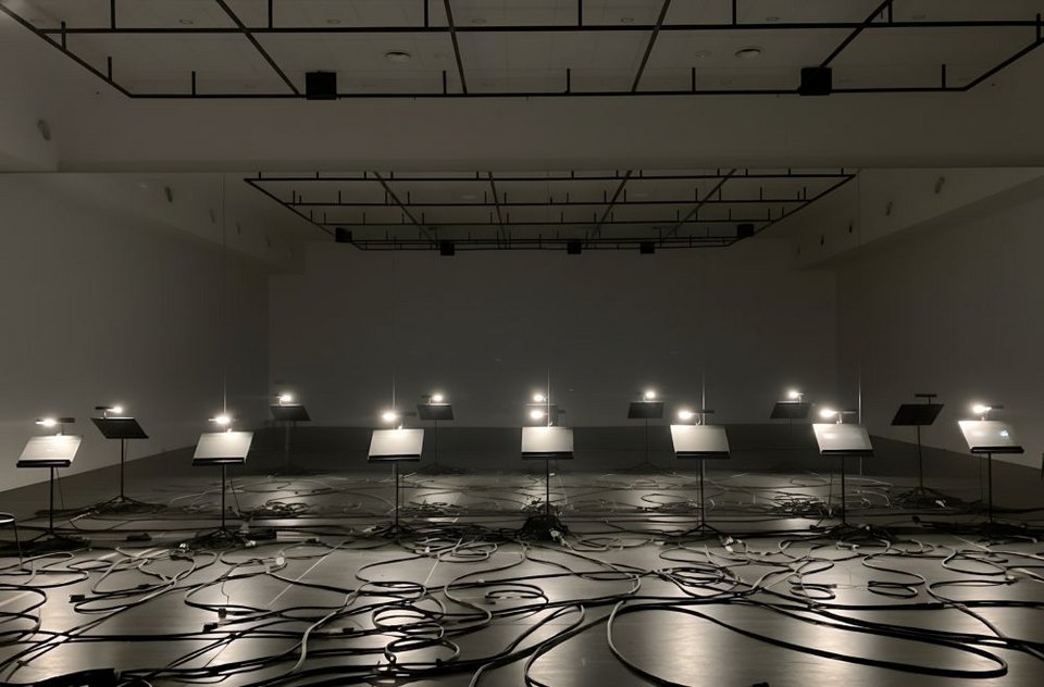 Από ένα κλειστό υπόγειο του κτιρίου του Μεγάρου, σε έναν κρυφό διάδρομο, σε μια αποθήκη σκηνικών και τέλος στην αίθουσα δοκιμών μπαλέτου, η δράση ξεδιπλώνεται αποσπασματικά ως ένα κειμενικό και μουσικό chat/συνομιλία μεταξύ καλλιτέχνη και ΤΝ