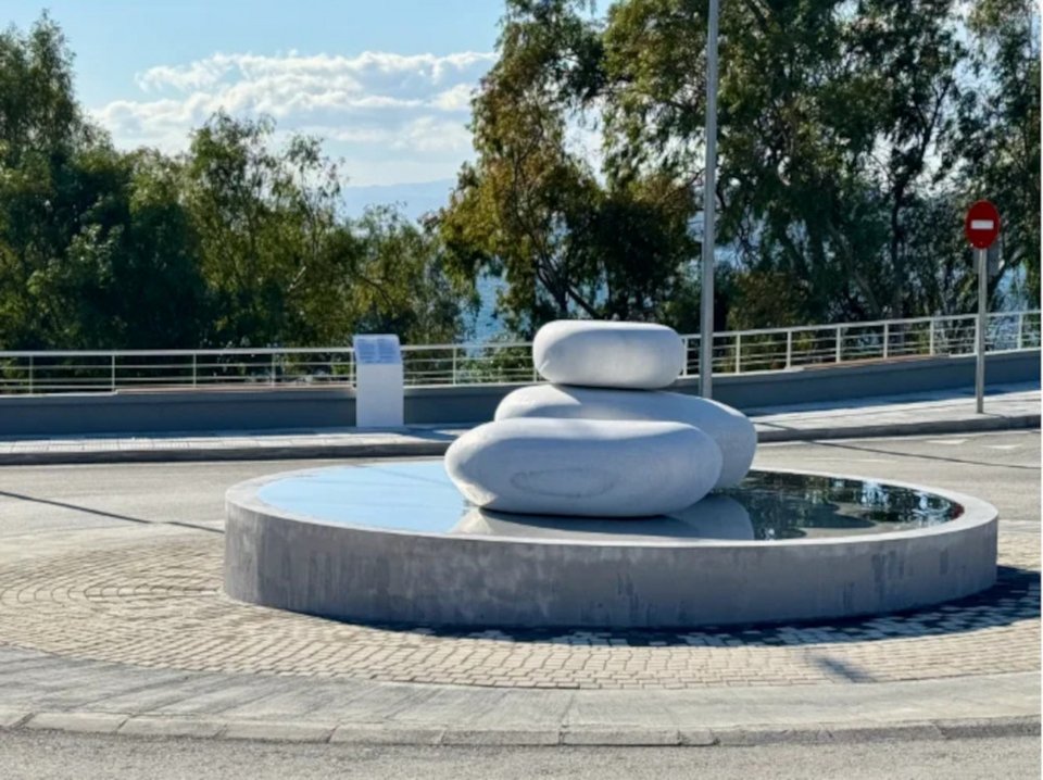 Το γλυπτό της Βένιας Δημητρακοπούλου είναι κατασκευασμένο από λευκό μάρμαρο της Νάξου και ανοξείδωτο χάλυβα, παραπέμποντας μορφολογικά στα χαρακτηριστικά βότσαλα της εμβληματικής παραλίας «Λαλάρια»