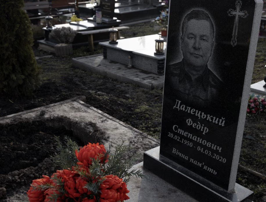 Στο νεκροταφείο, το χώμα είναι ακόμη φρέσκο. Ο ξύλινος σταυρός έχει σπάσει και στέκεται στο πλάι, μαζί με μια μεταλλική πινακίδα βαμμένη στα χρώματα της ουκρανικής σημαίας / FACEBOOK