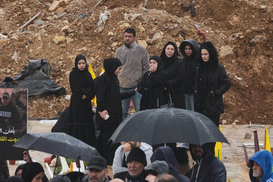 Πενθούντες συγκεντρώνονται κοντά σε έναν φρεσκοσκαμμένο τάφο κατά τη διάρκεια της κηδείας των 3 λιβανέζων δημοσιογράφων, σε προσωρινό νεκροταφείο στη Νταχίγιε, στα νότια προάστια της Βηρυτού / Φωτογραφία: AP / Hassan Ammar   